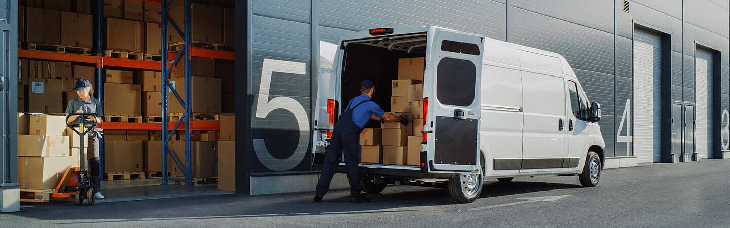 Mężczyzna ładujący pudła do furgonetki przed magazynem.